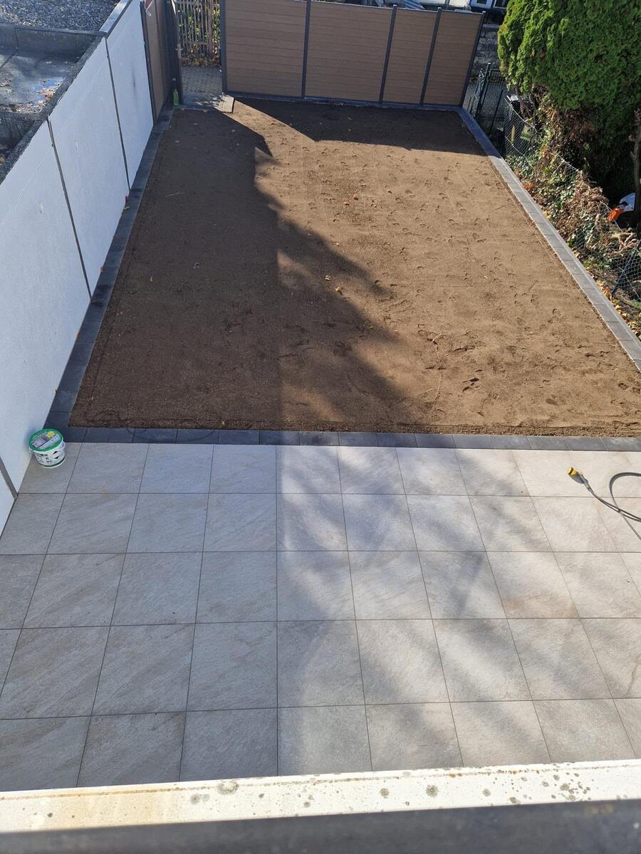 Neu verlegte helle Feinsteinzeug-Terrassenplatten mit angrenzender, vorbereiteter Rasenfläche