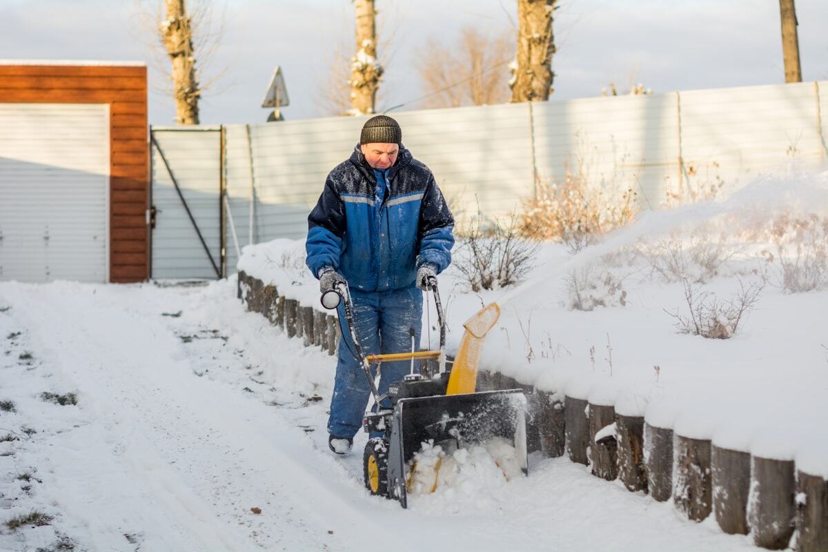 Schneefräse räumt einen verschneiten Weg entlang eines Grundstücks